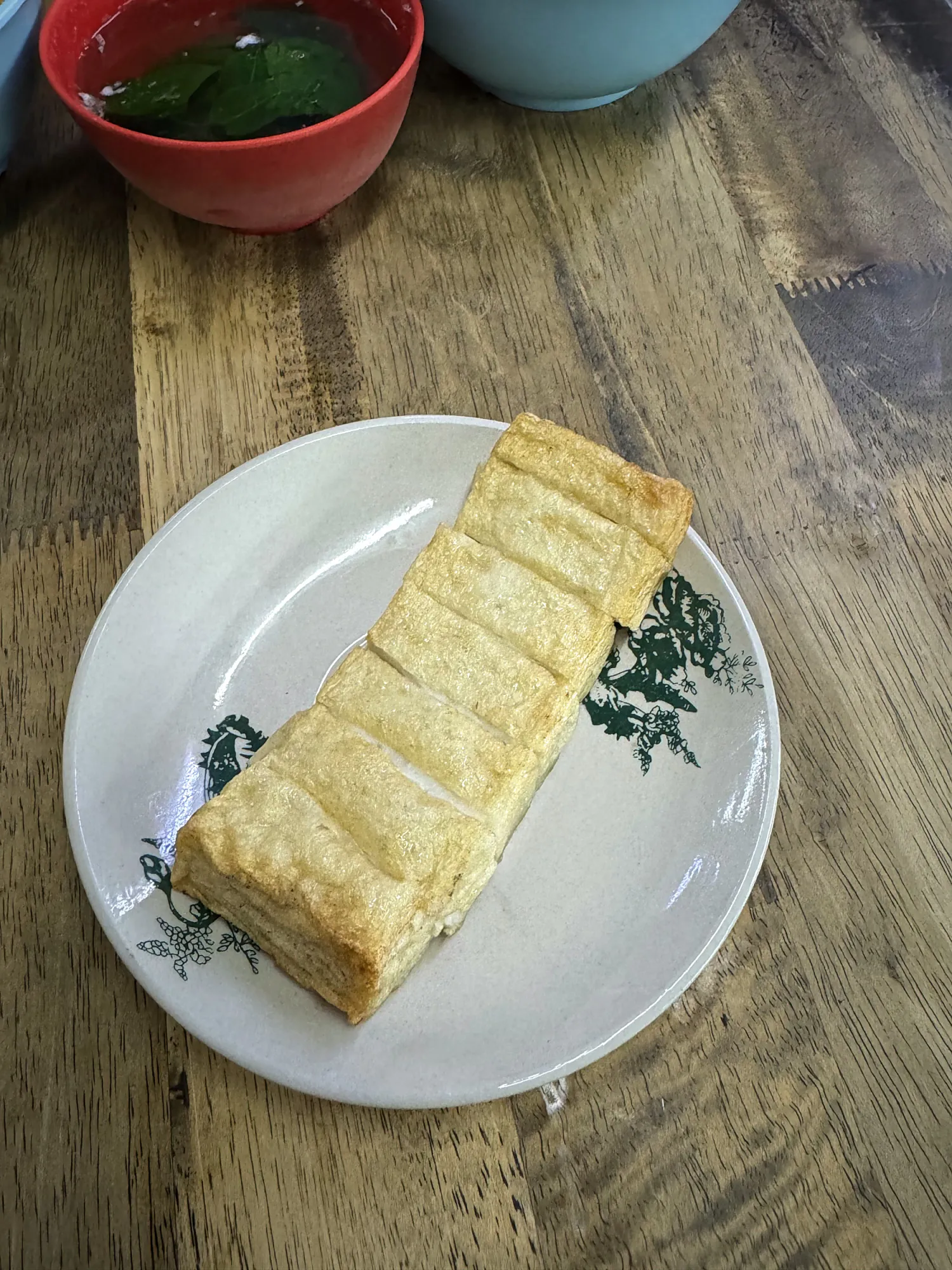 A sliced block of fishcake on a white plate with green patterns at Kin Kin in Kuala Lumpur.