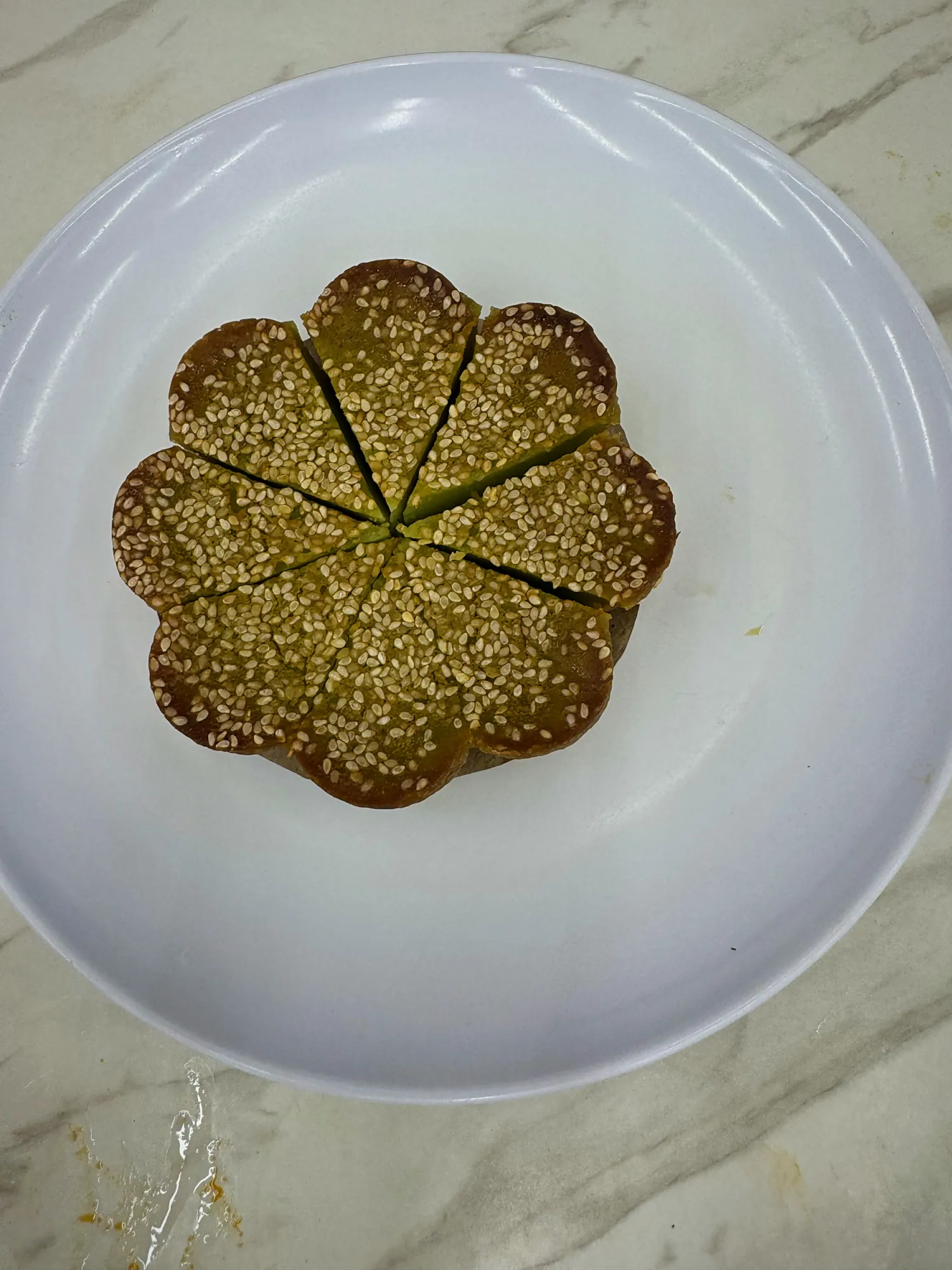 A flower-shaped kuih bakar pandan covered in white sesame seeds and cut into slices on a white plate at Wanjo.