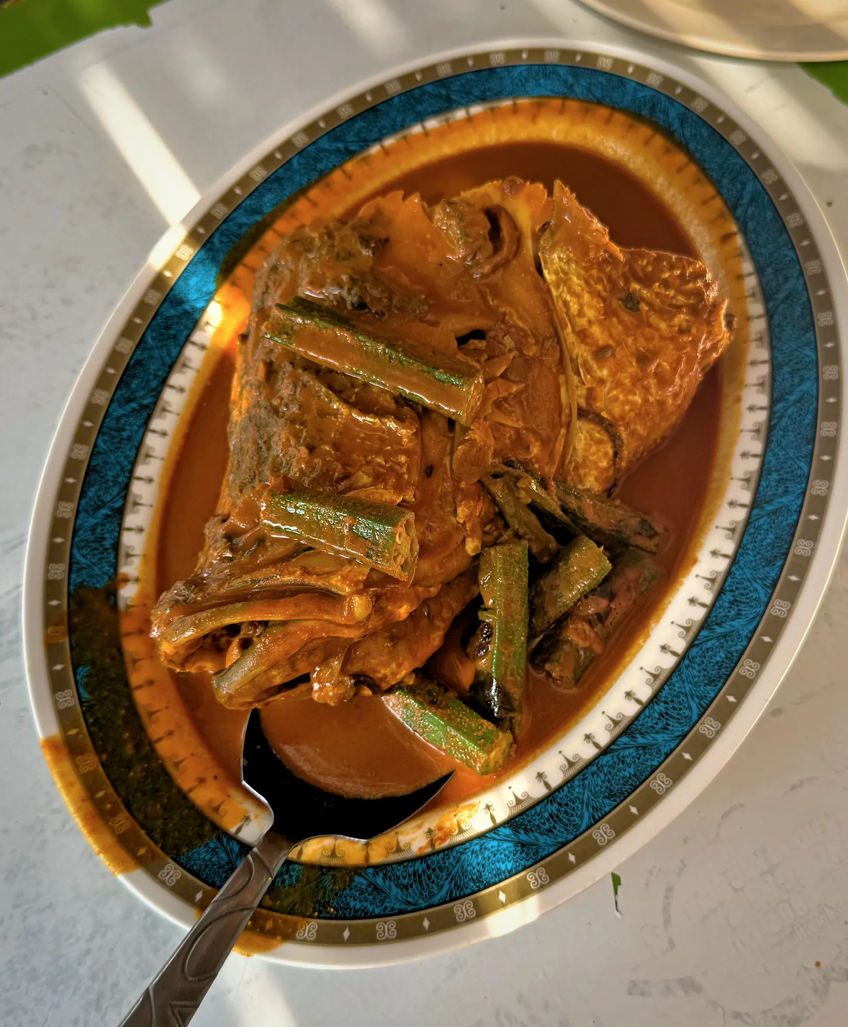 Overhead view of fish head curry with okra in a spiced gravy on an ornate plate at Anuar's Fish Head Curry in Kuala Lumpur