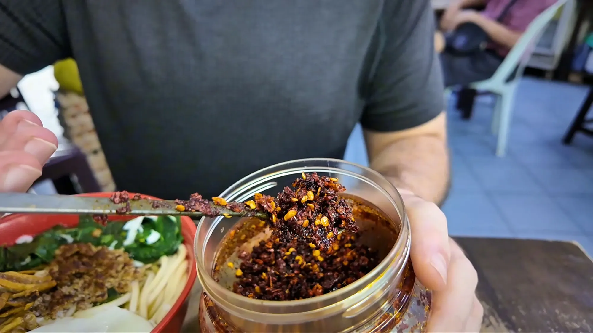 Scooping dried chili flakes from the table jar onto a bowl of chili pan mee at Kin Kin, Kuala Lumpur.