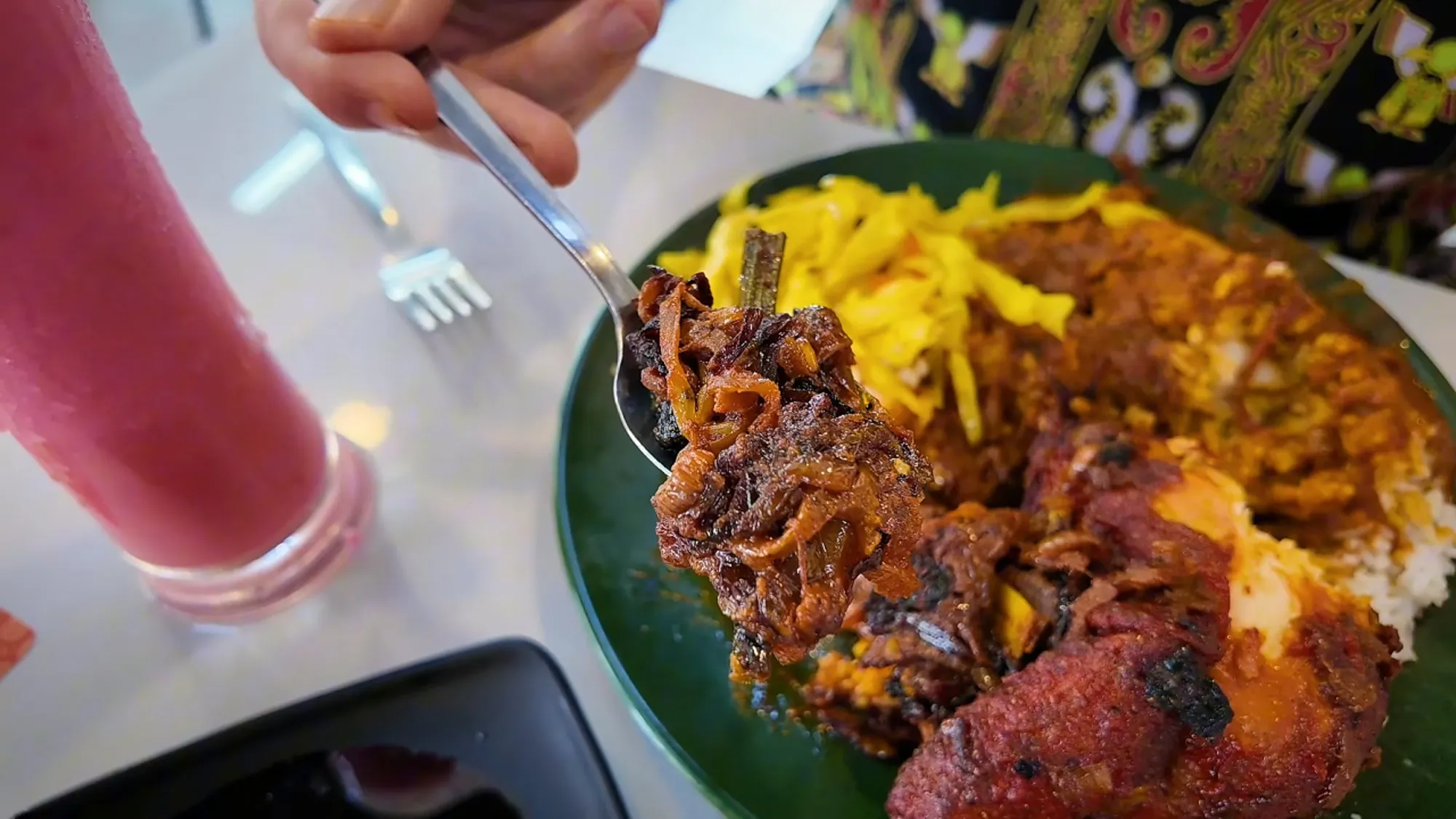 A spoonful of caramelized onions lifted from a plate of nasi kandar with fried chicken and yellow cabbage at Line Clear, Kuala Lumpur.