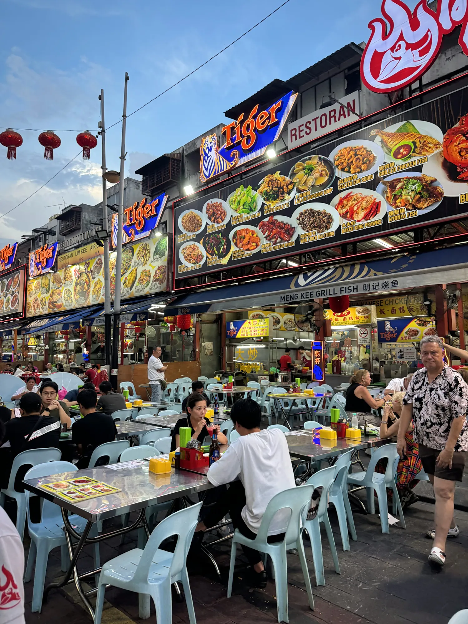 Restaurant signs with photo menus above outdoor tables on Jalan Alor, Kuala Lumpur.