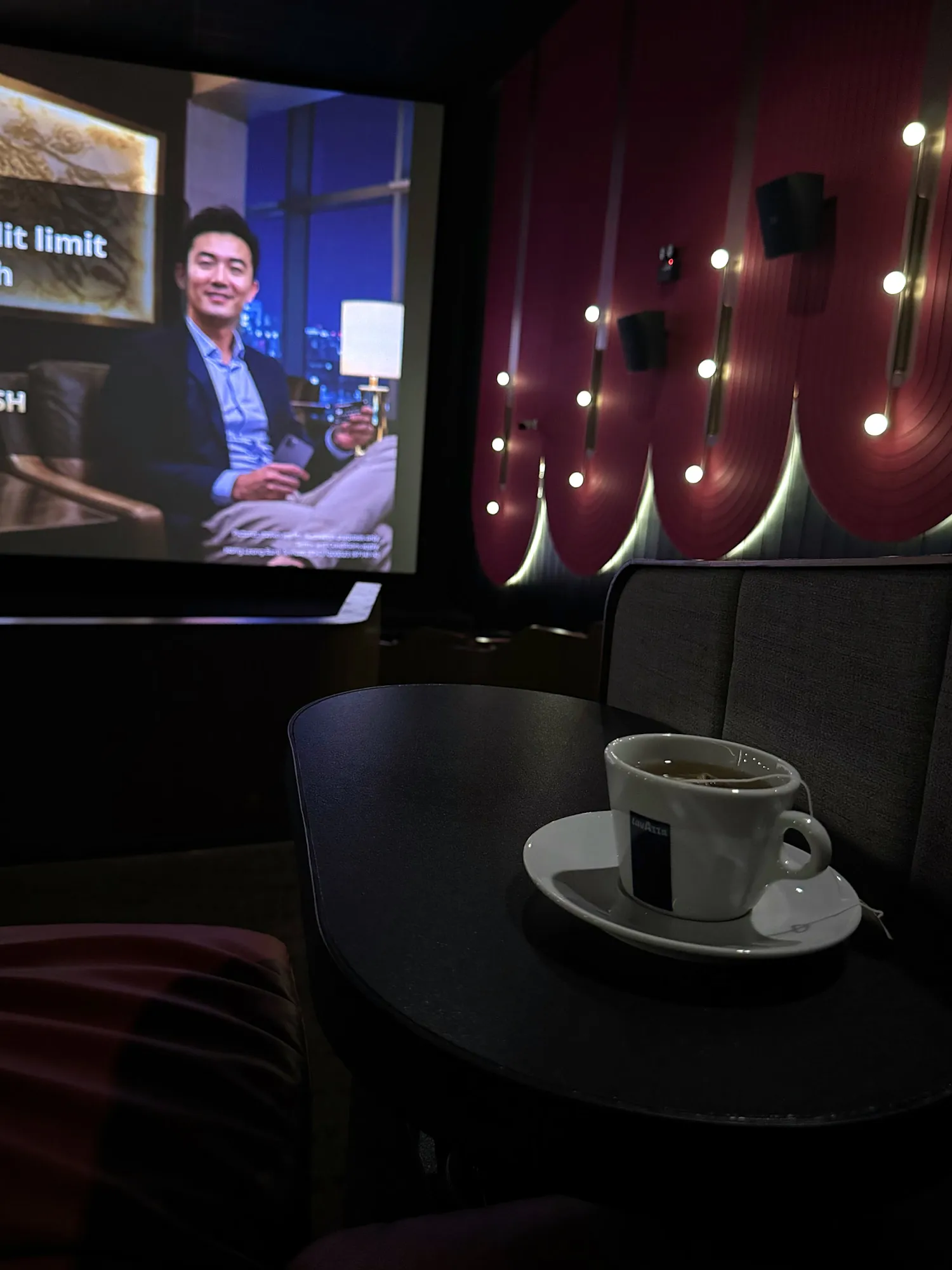A cup of tea on the side table in a Maybank Comfort Cabin at Aurum Theatre, Kuala Lumpur, with the movie playing.