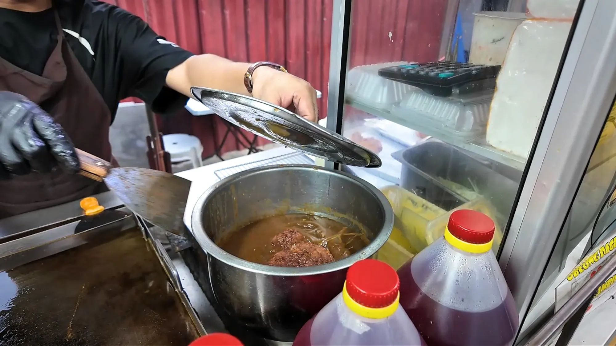 A cook lifts the lid off the steel pot of brown gravy that the patties soak in at Boss Burger, Jalan Alor, Kuala Lumpur