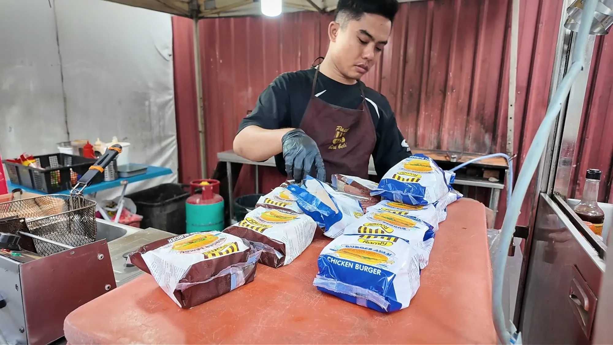 A Boss Burger cook lines up burgers wrapped in Ramly-branded paper on the counter, Jalan Alor, Kuala Lumpur