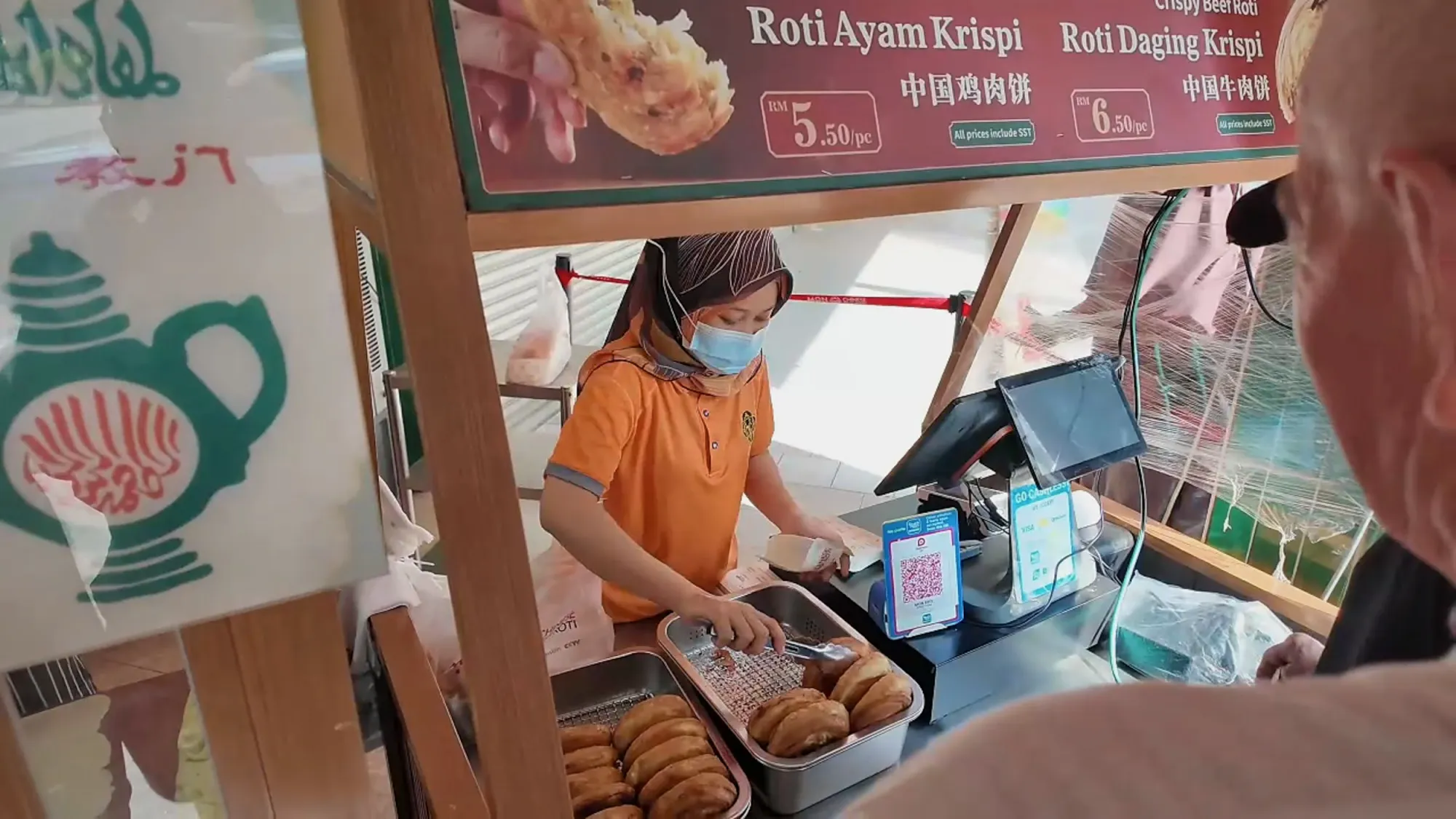 A server at the Mon Chinese Beef Roti counter handing over fresh roti under the menu board.