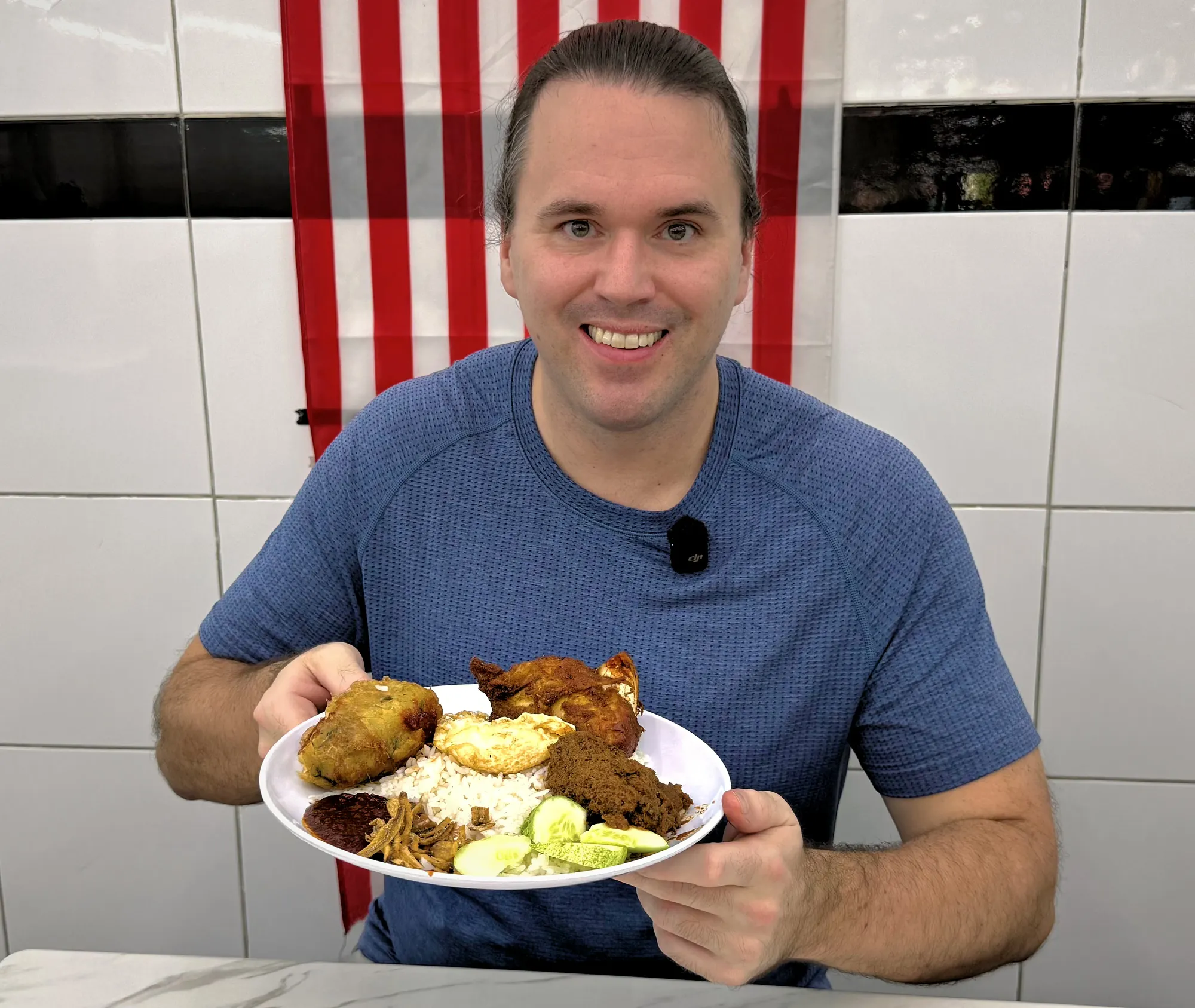 Cream smiling and holding up a plate of nasi lemak with fried chicken, beef rendang, and begedil at Nasi Lemak Wanjo in Kampung Baru, Kuala Lumpur.