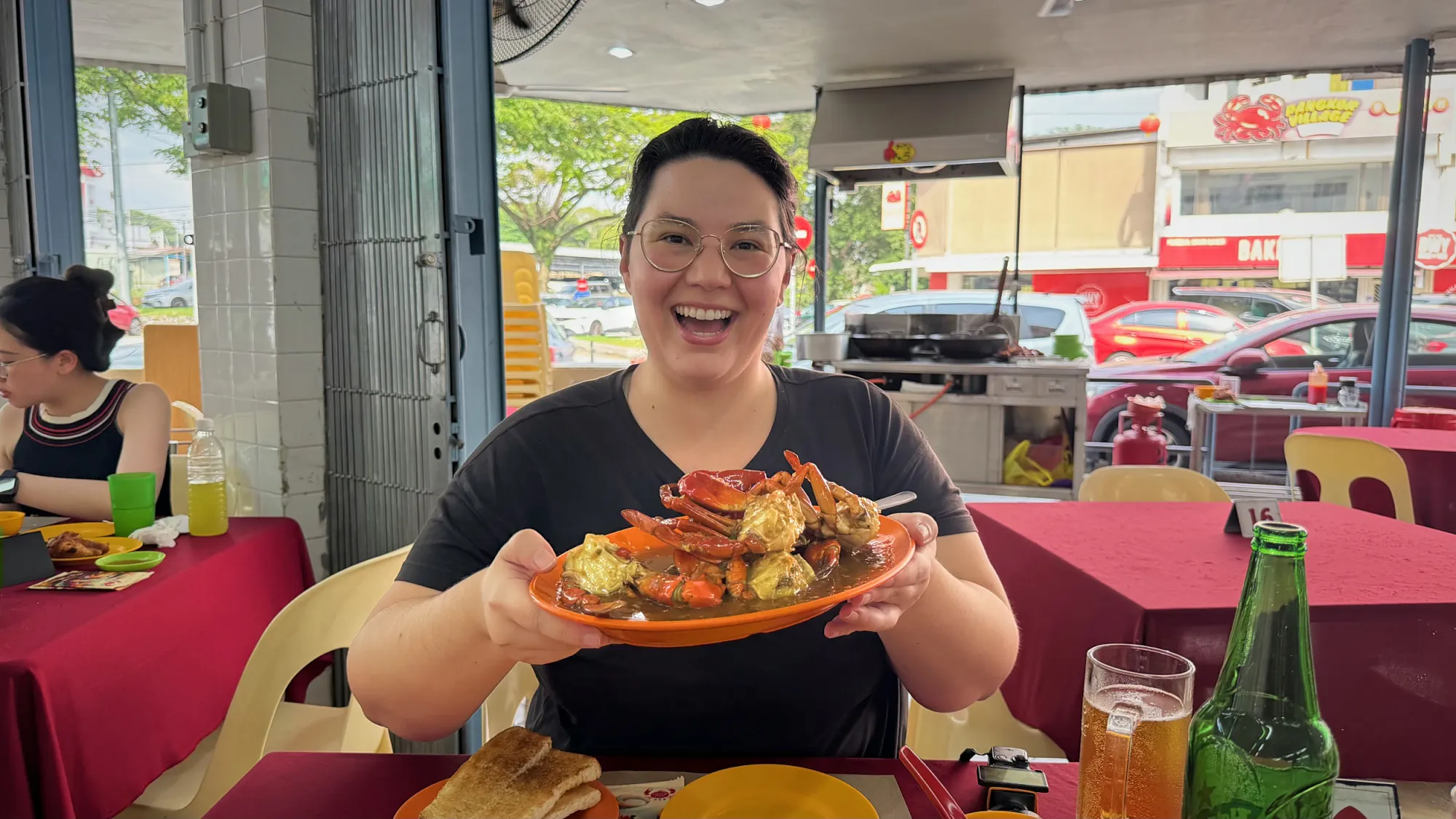 Smiling and holding up a plate of chilli crab at a red-clothed table in Restoran Fatty Crab, Petaling Jaya.