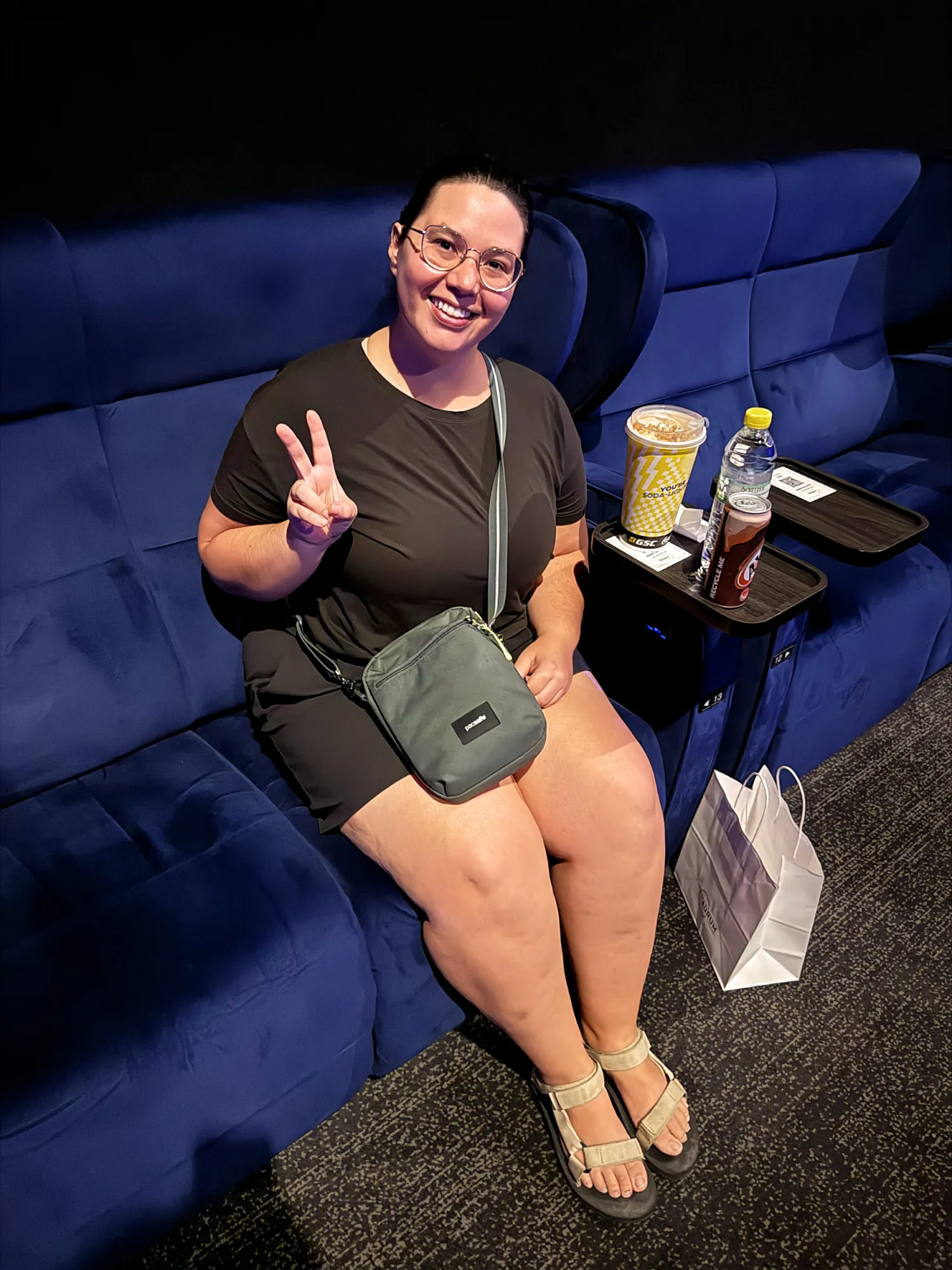 Bernie making a peace sign from a blue velvet IMAX recliner with drinks on the tray at Aurum Theatre, Kuala Lumpur.
