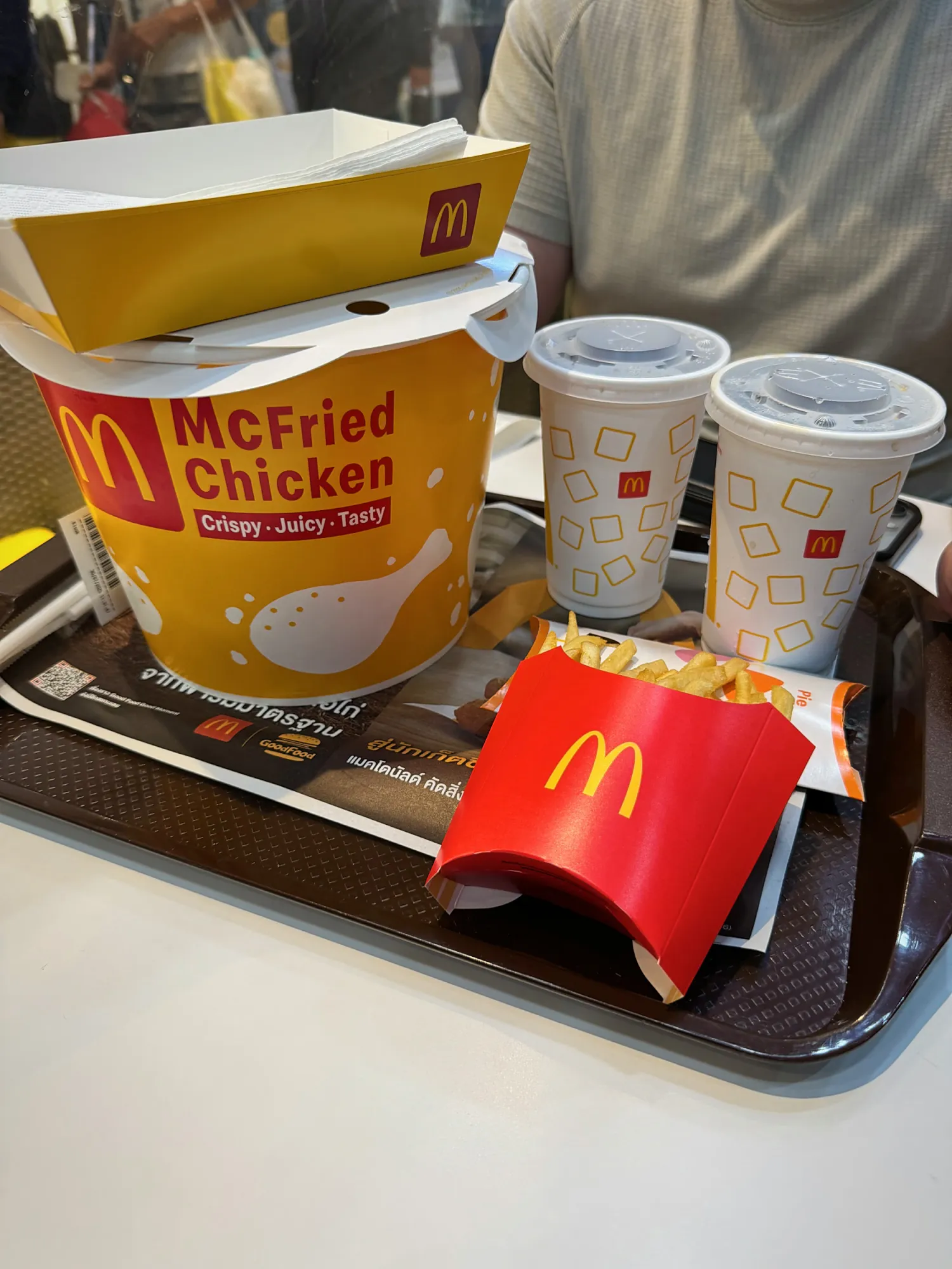 A McFried Chicken box with fries and two drinks on a tray at McDonald's in Bangkok, Thailand.