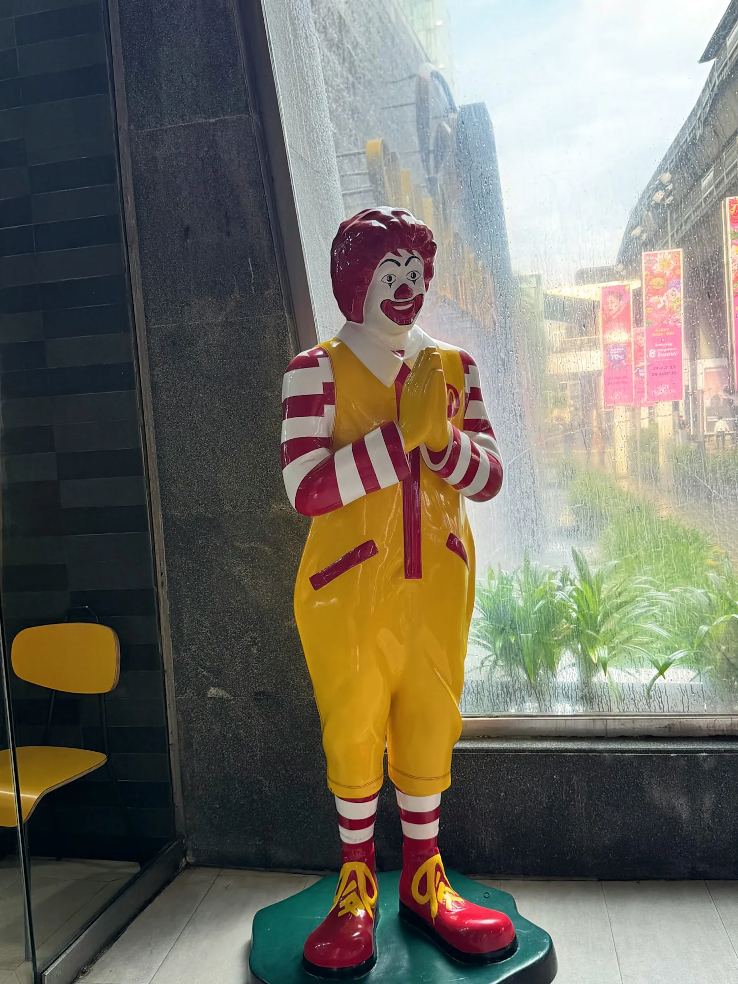 A Ronald McDonald statue with palms pressed together in a wai greeting at the entrance of a McDonald's in Bangkok, Thailand.