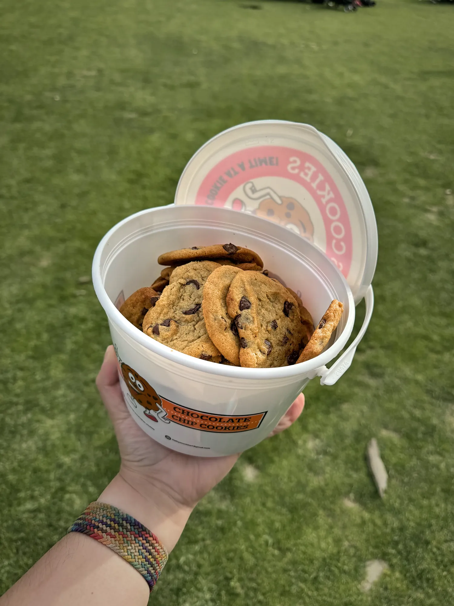 A hand holding an open bucket of chocolate chip cookies over the grass at Pokémon GO Tour at the Rose Bowl.
