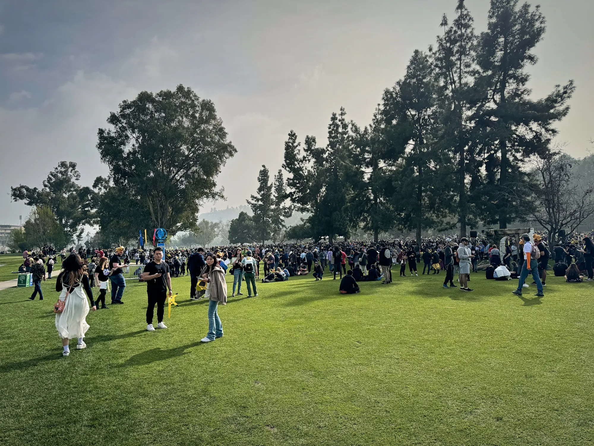 Pokémon GO players spread across a wide lawn under tall pine trees at the Rose Bowl during GO Tour.