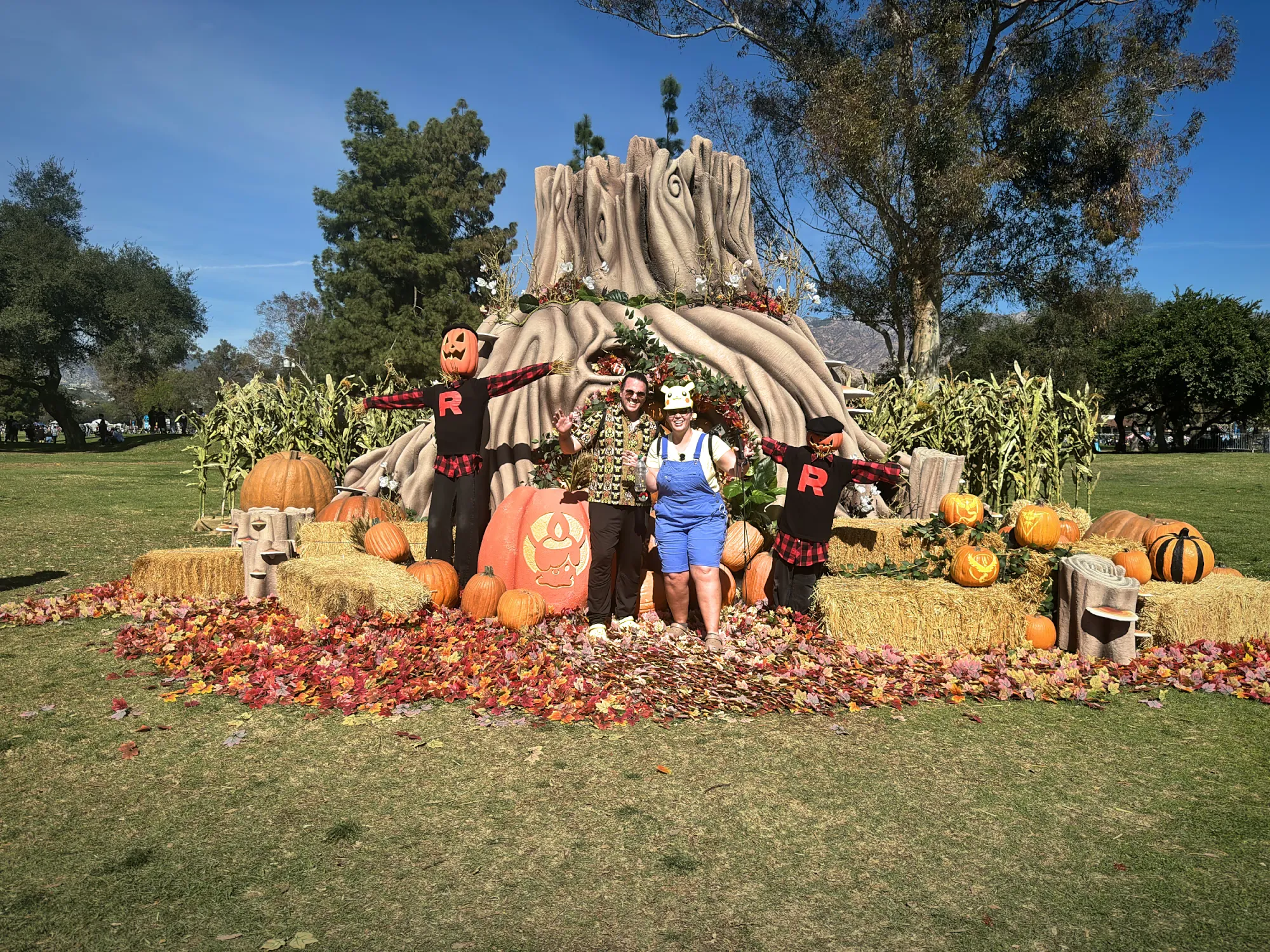 Bernie and Cream standing among pumpkins, hay bales, and Team Rocket scarecrows at the autumn habitat of Pokémon GO Tour Unova in Pasadena.
