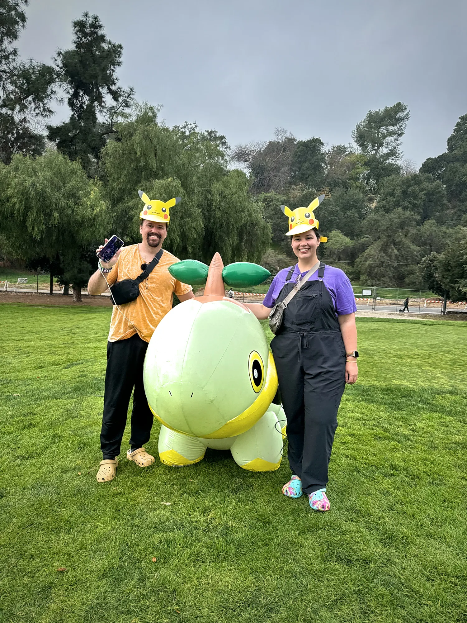Bernie and Cream in Pikachu hats beside a giant inflatable Turtwig at Pokémon GO Tour Sinnoh in Pasadena, one of them holding up a phone.
