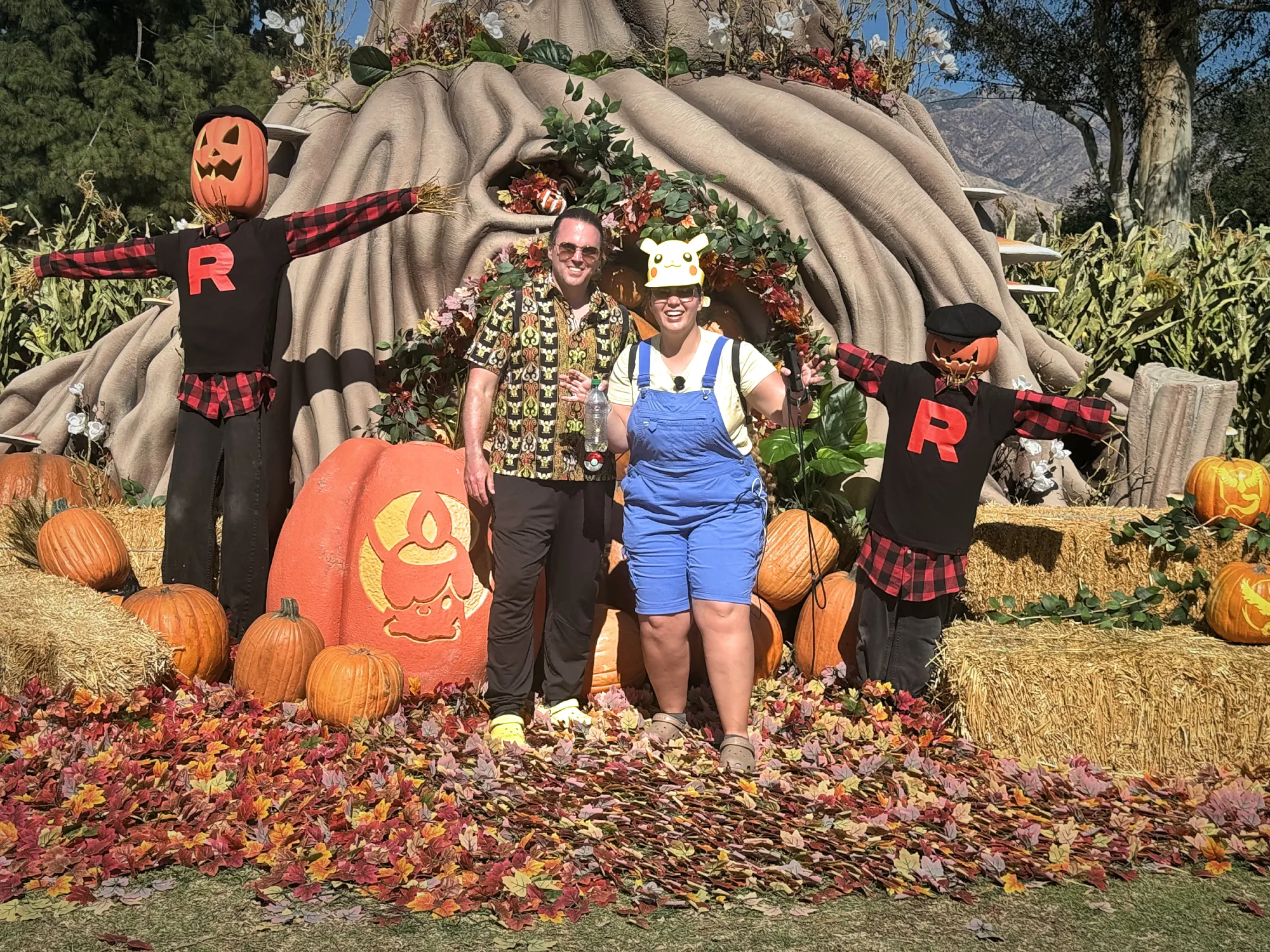 Bernie and Cream posing between Team Rocket scarecrows and Pokémon pumpkins at the autumn habitat of Pokémon GO Tour Los Angeles at the Rose Bowl.