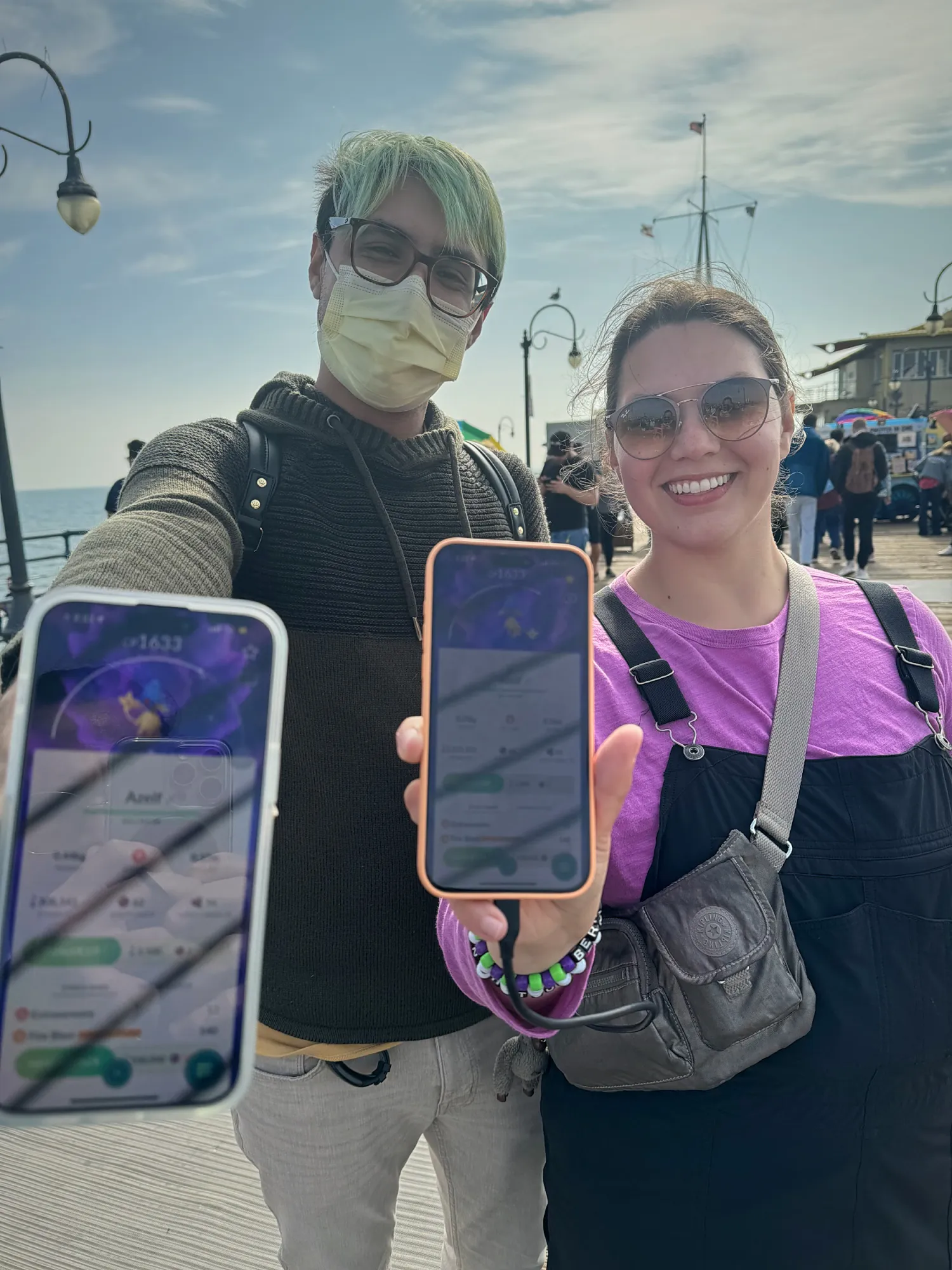 Two friends hold up their phones showing Pokémon GO catches on the Santa Monica Pier on a sunny day.
